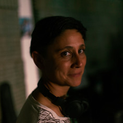 Jessica Candal, mulher de cabelos escuros presos, em retrato com iluminação suave, olhando levemente para a câmera.